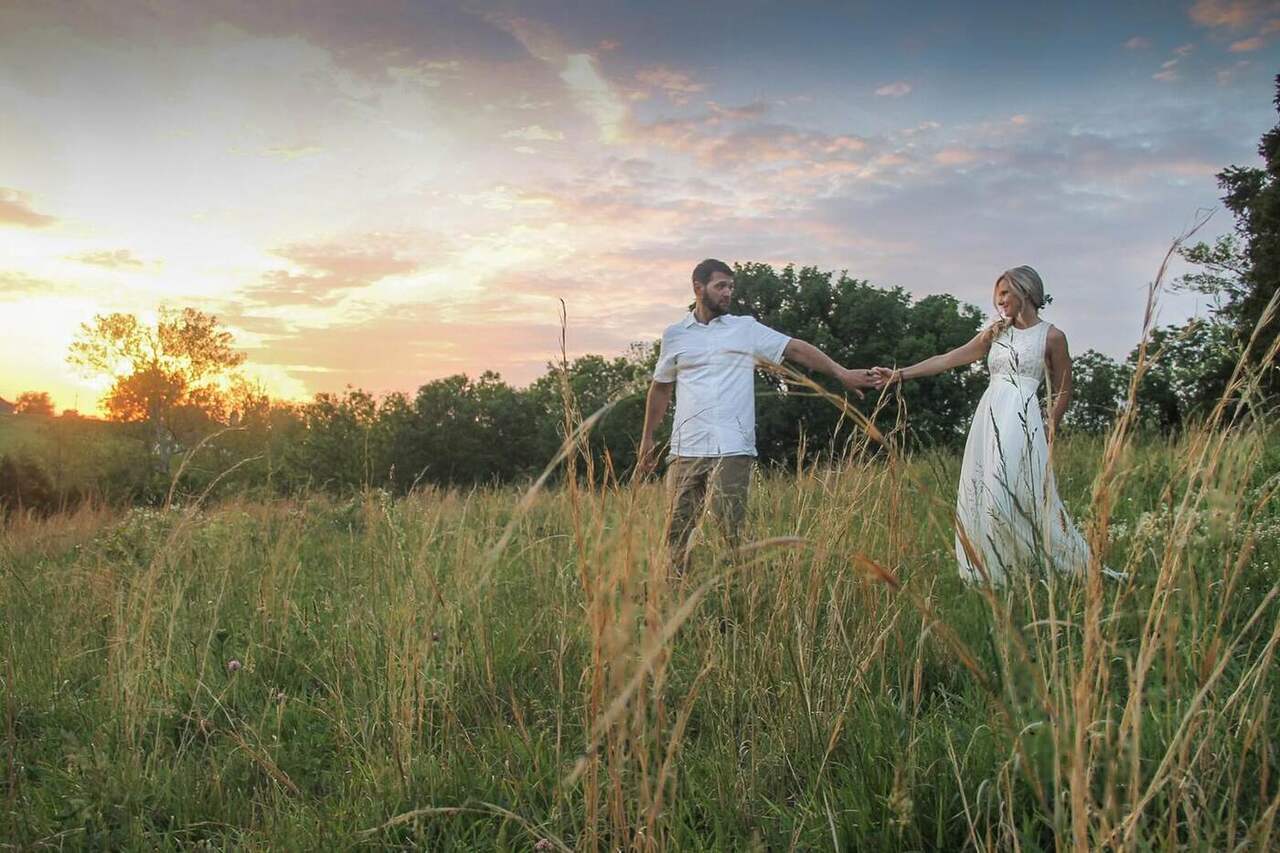 A couple holding hands in the tall grass at sunset