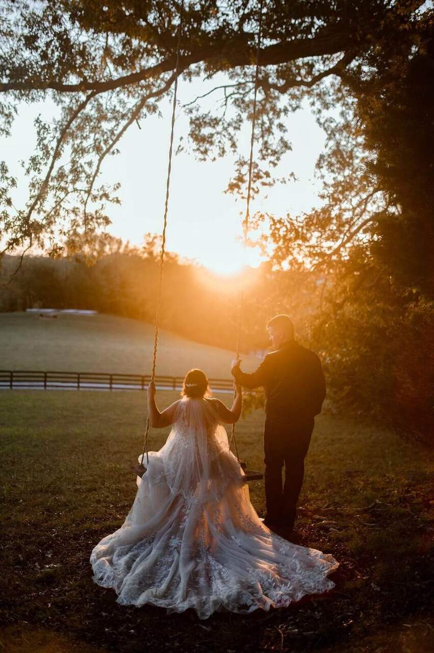 Bride on the rope swing at sunset with the groom beside her